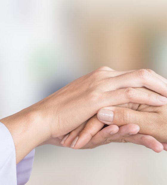 femaledoctorhandcomfortingpatientwithblurbackgroundofhospitalroom